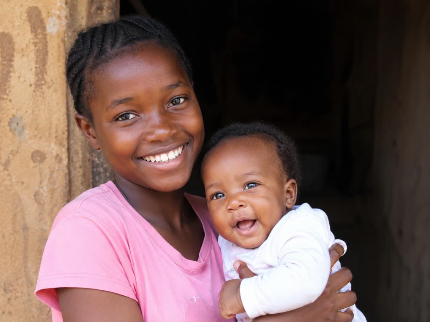 Young girl in pink holding her smiling baby — hope and new beginnings