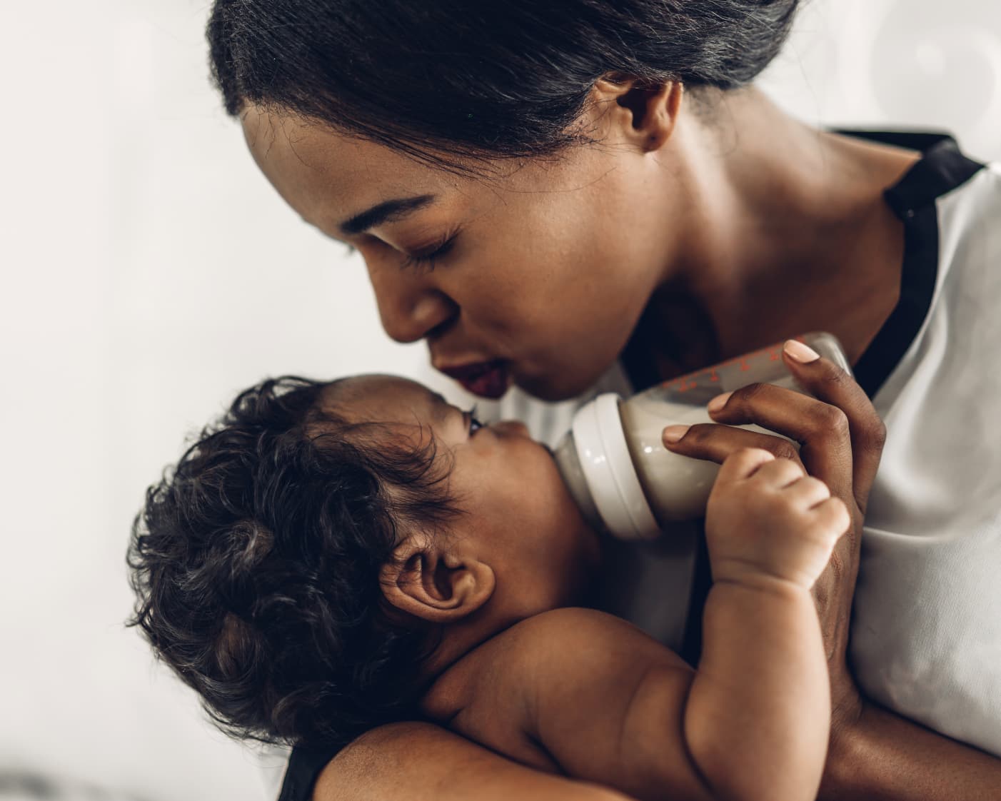 Mother kissing baby while bottle feeding — tenderness and care